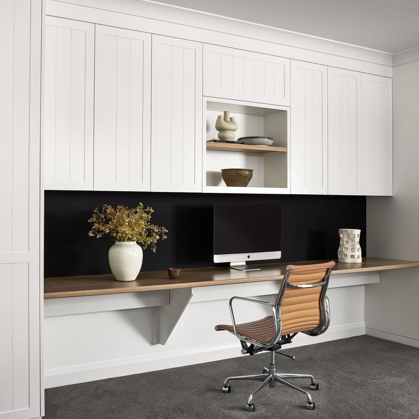 White-panel storage wall with a wooden desk, computer, and decorative pieces in a modern home office.